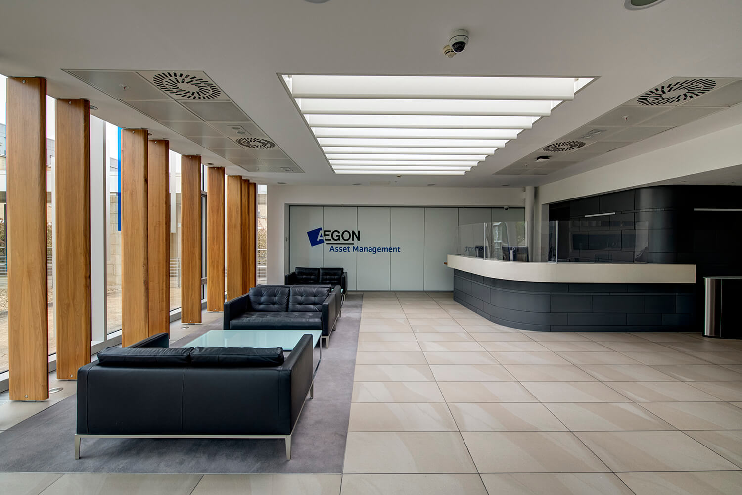 Interior photography of office reception by Edinburgh Photographer Blink Imaging. You can see leather sofas on the left hand side by a modern window. There is a modern skylight above this. The reception desk is on the right hand side. The space is very modern with straight linear lines.